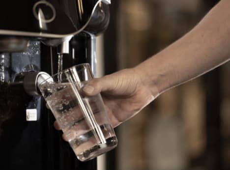 A man filling glass of water from the dispenser.